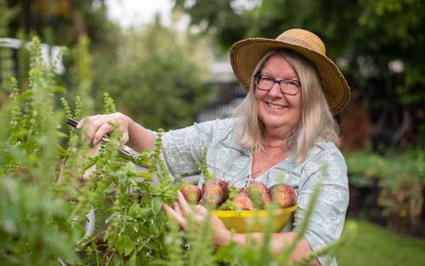 A woman smiling while picking vegetables from her garden | Icon Cancer Centre